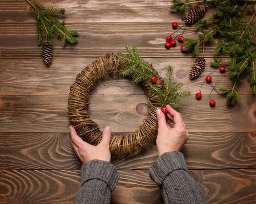 wicker wreath base with hands adding pine leaves against wooden background